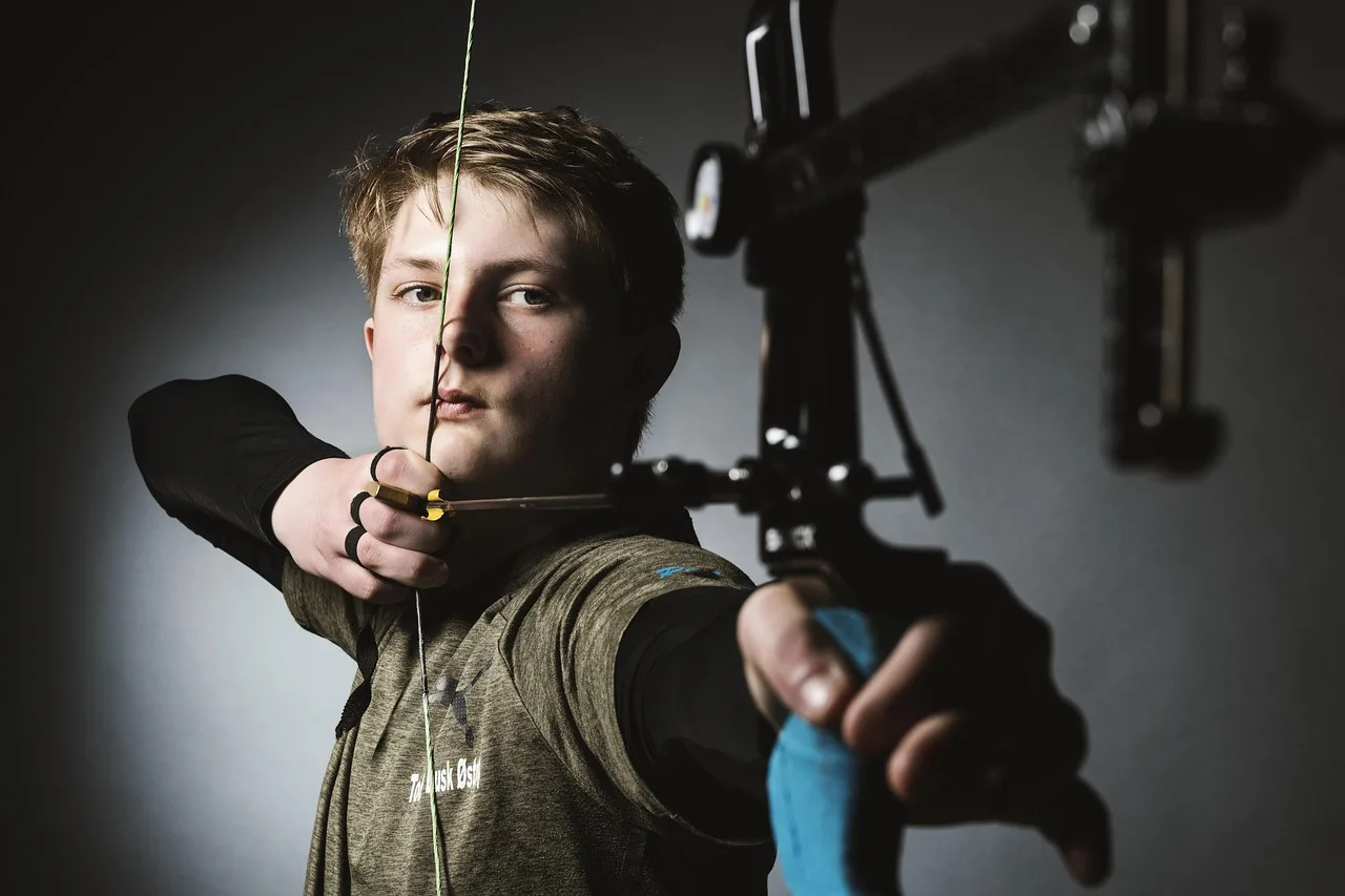 Parent helping a youth archer compare arrow shaft length to a drawn bow at an outdoor range