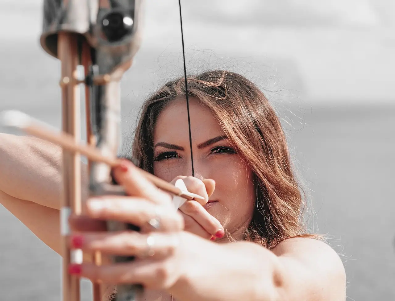 Archery competition sight on a recurve bow aimed at a distant target at an outdoor tournament