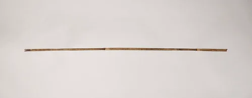 Traditional archer sorting wood arrow shafts beside a bow and measuring tools