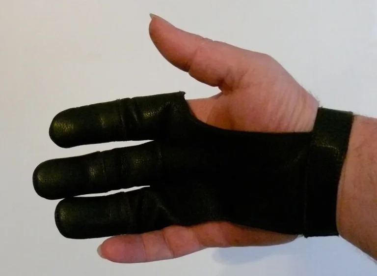 Leather and synthetic archery gloves beside a bow on a bench at an outdoor range