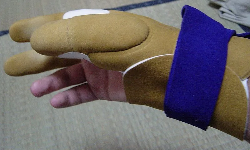 Close-up of a synthetic archery glove under string tension, showing fingertip compression and seams