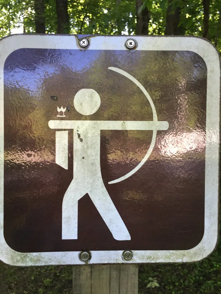 Recurve archer at an outdoor range with an archery face mask resting nearby