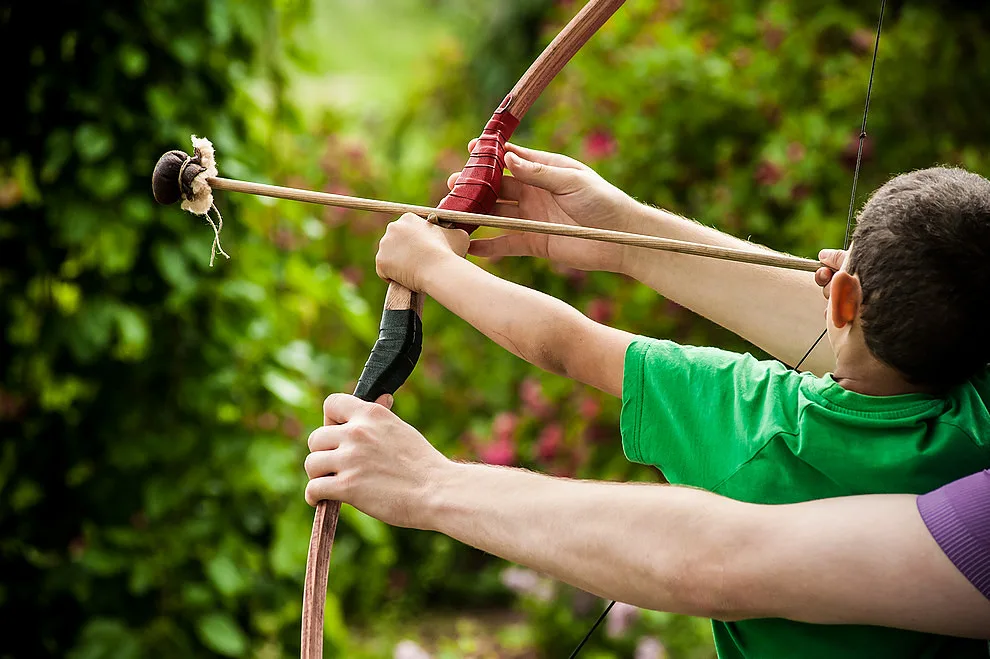 Archer at an outdoor range comparing a finger release and mechanical release with targets behind