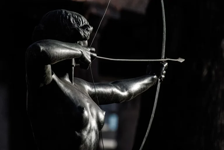 Archer comparing two arrows beside a compound bow at an outdoor range in natural morning light.