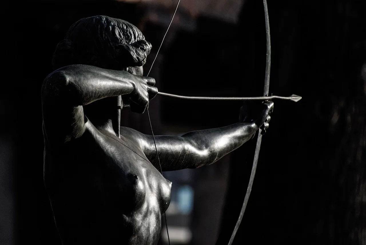 Archer comparing two arrows beside a compound bow at an outdoor range in natural morning light.
