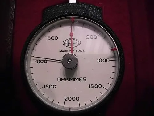 Hands testing a carbon arrow shaft on a spine tester in close-up.