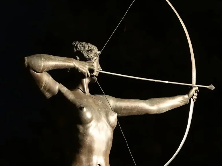 Woman archer comparing an arrow and bow setup at an indoor range, with charts and equipment nearby