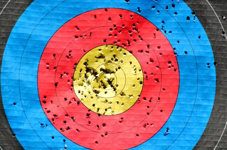 Archer wearing clear archery safety glasses at an outdoor range with a bow drawn