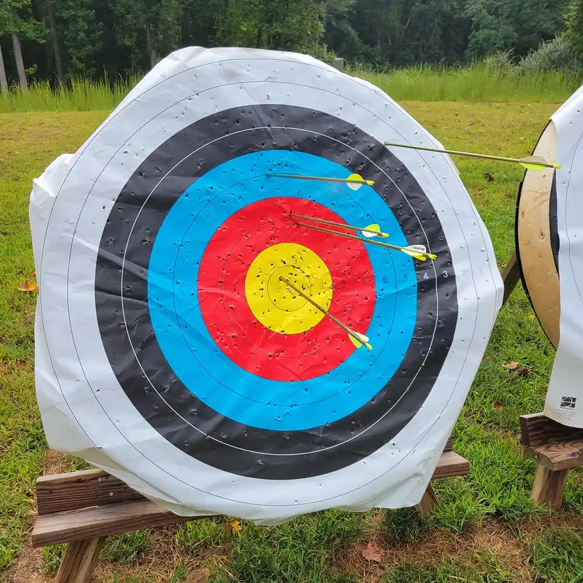 Hand marking an archery scorecard on a clipboard beside a pen