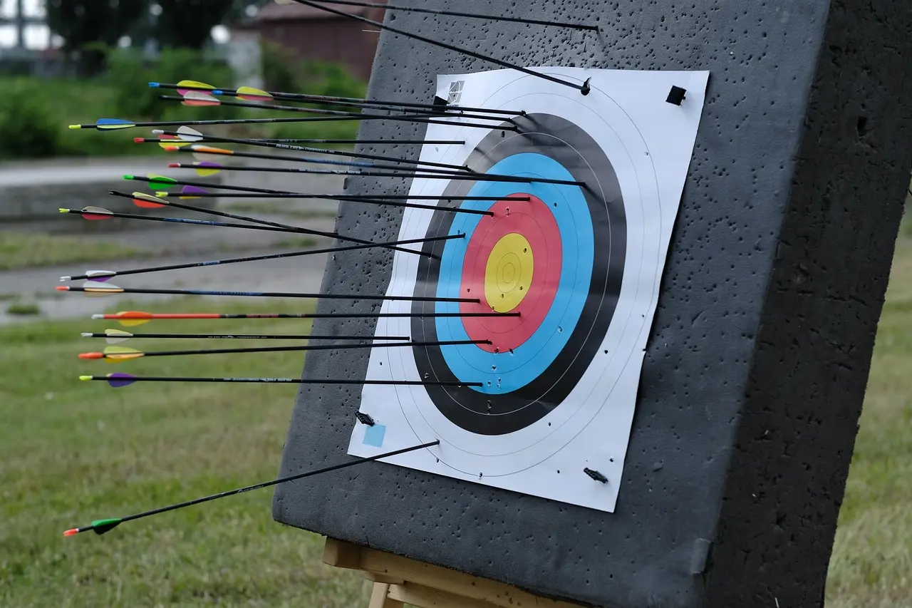 An adult hands a boxed archery target to a teen in a backyard practice area.