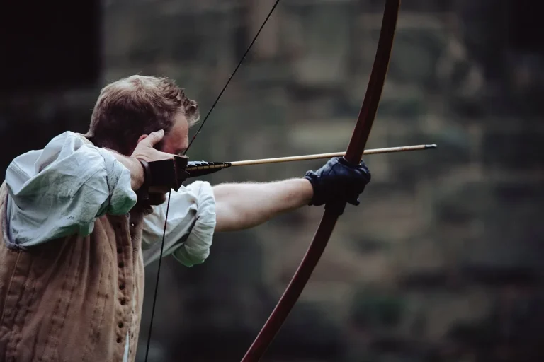 Competition bow setup laid out on a bench with recurve bow, arrows, and accessories at an outdoor range