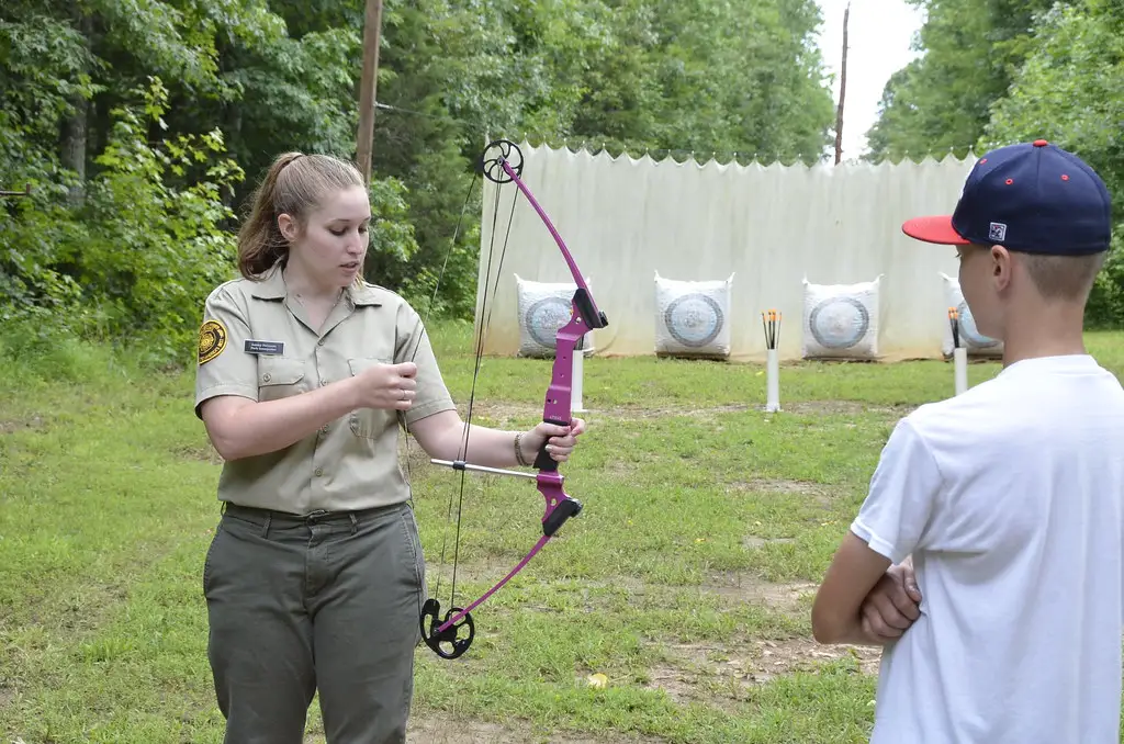 Hands adjusting a compound bow's draw length setting with an Allen wrench.