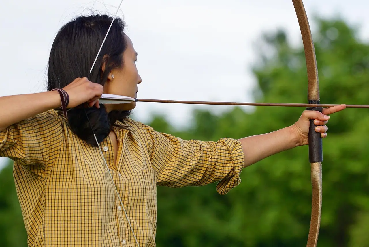 An archer aiming on an outdoor range with targets at different distances and an arrow in flight.