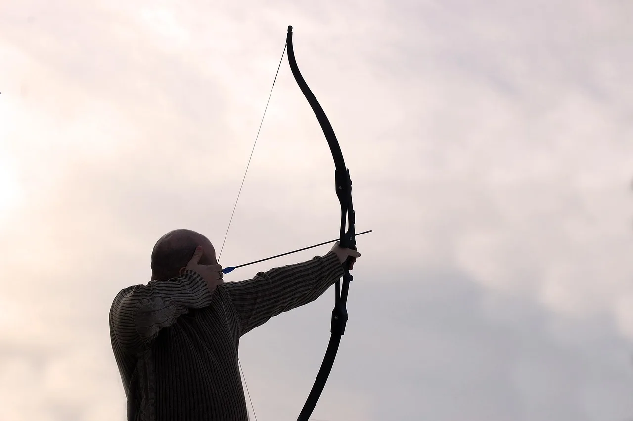 Archer measuring a recurve bow with a tape measure on a workbench