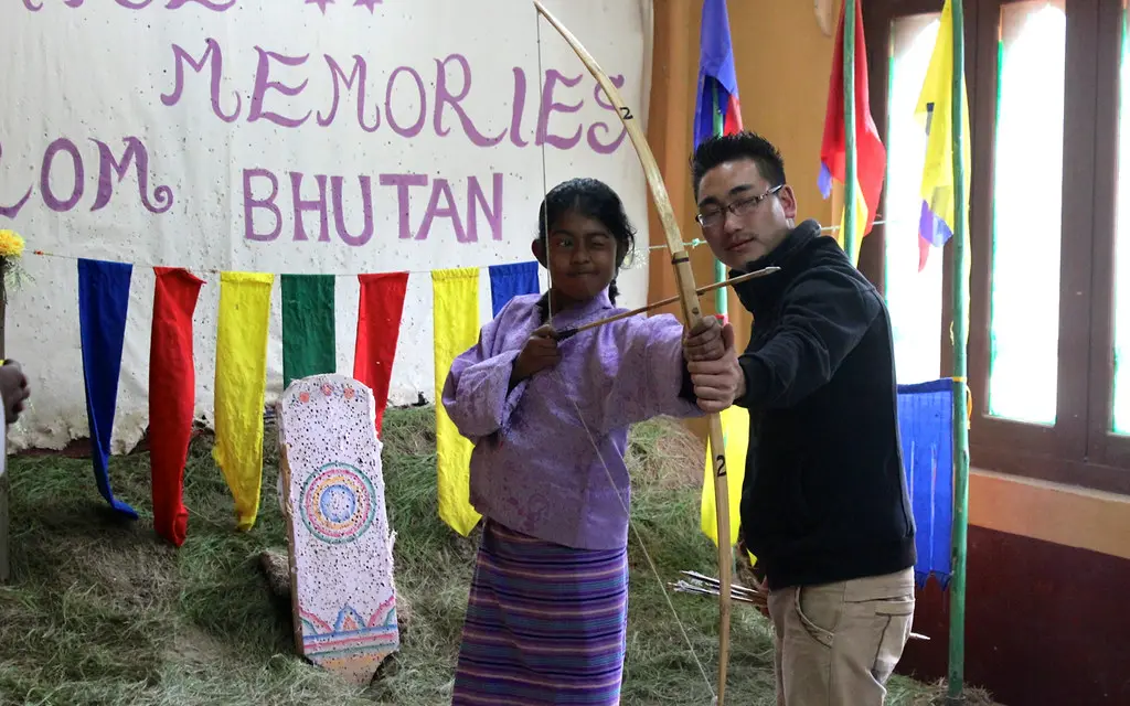 Beginner archer at an outdoor range drawing a recurve bow while a coach checks form