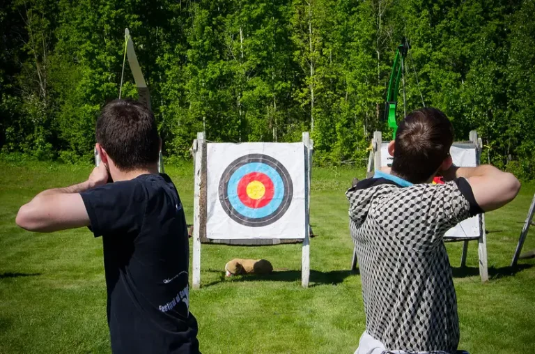 Beginner archer holding a recurve bow at an outdoor range with targets in the background