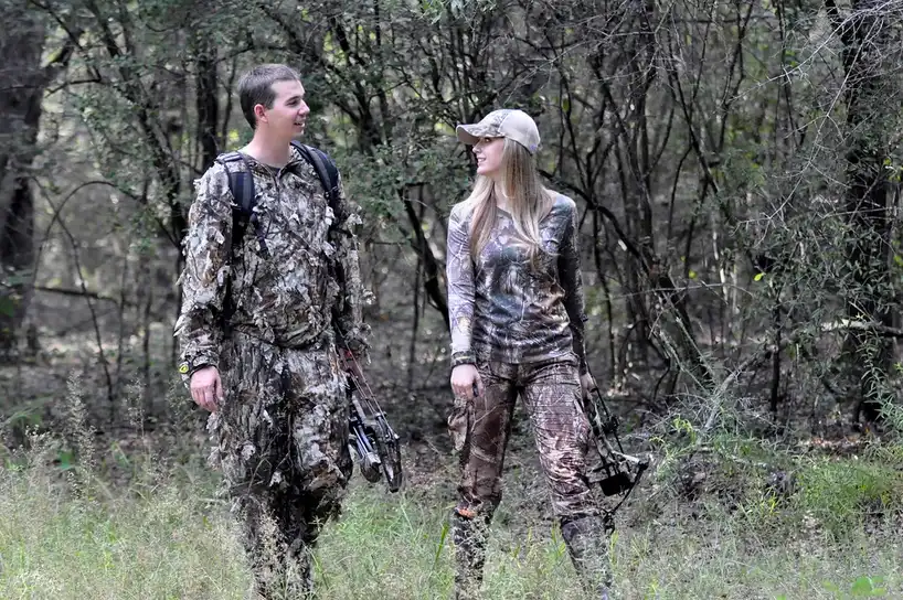 Close-up of camouflage fabric, gloved hands, and a bow setup for bowhunting