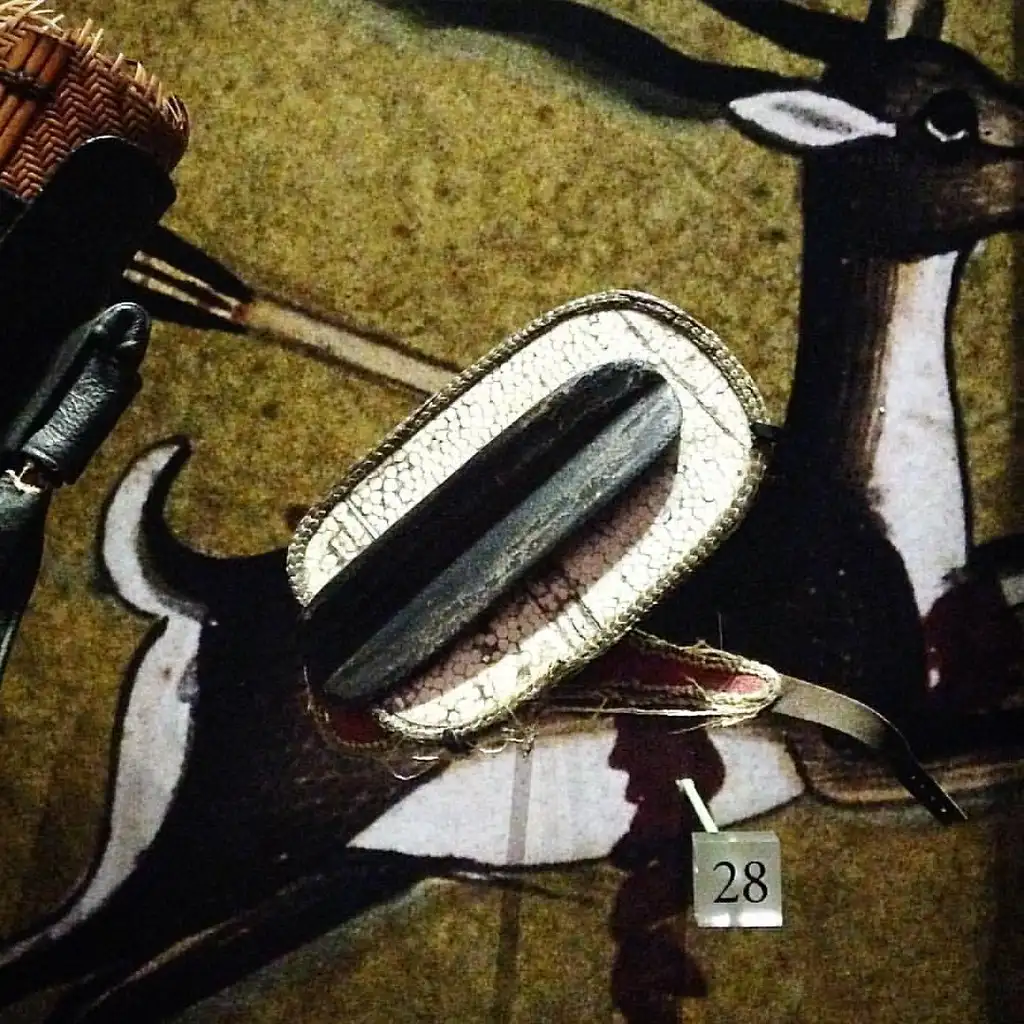 Leather archery gloves and finger tabs laid out beside a recurve bow in natural light
