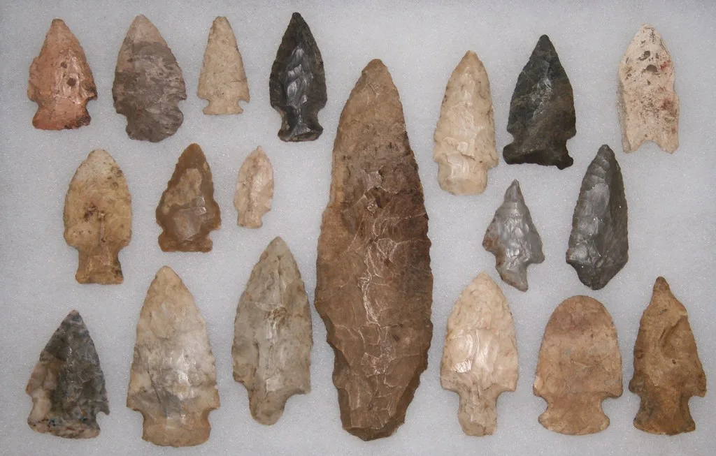 Stone arrowheads beside a wooden bow and arrows on weathered hide in natural light